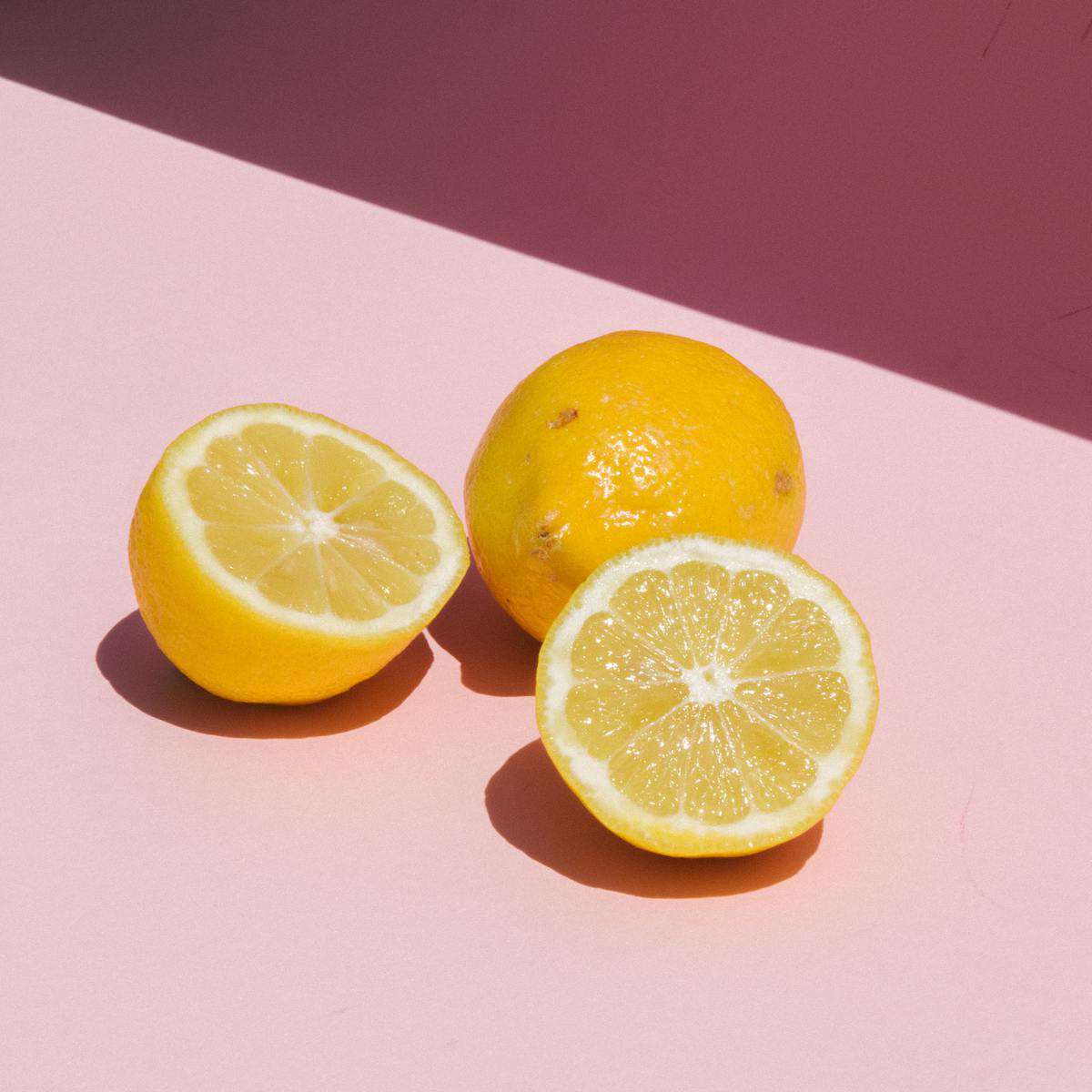 Two Lemons with one cut in half on a pink counter. 