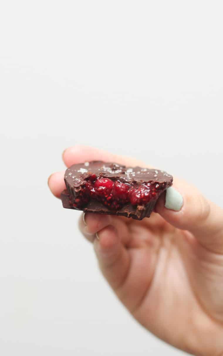 A hand holding up a chocolate cup with chia jam pouring out from the middle.