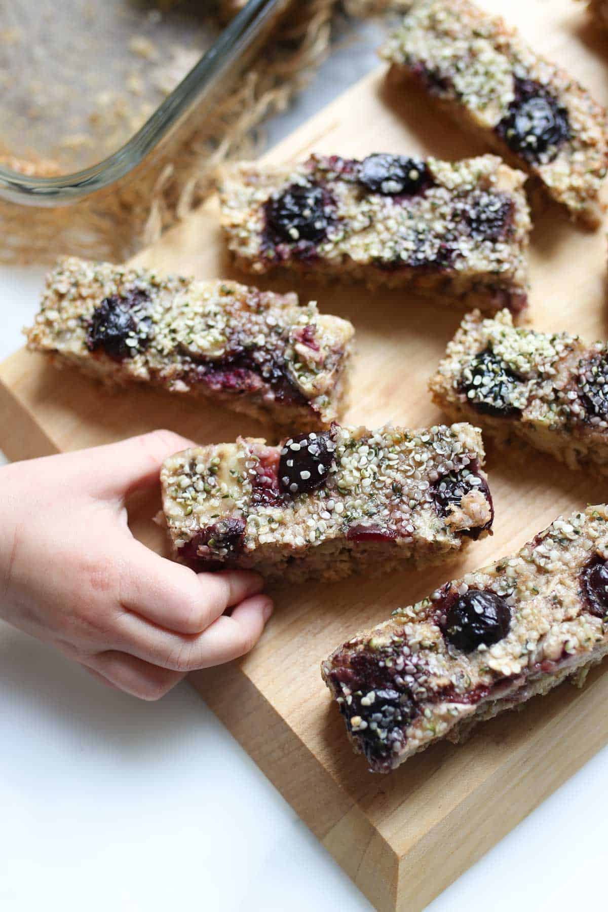 Toddler hand grabbing a banana baked oatmeal finger from a wooden cutting board. 