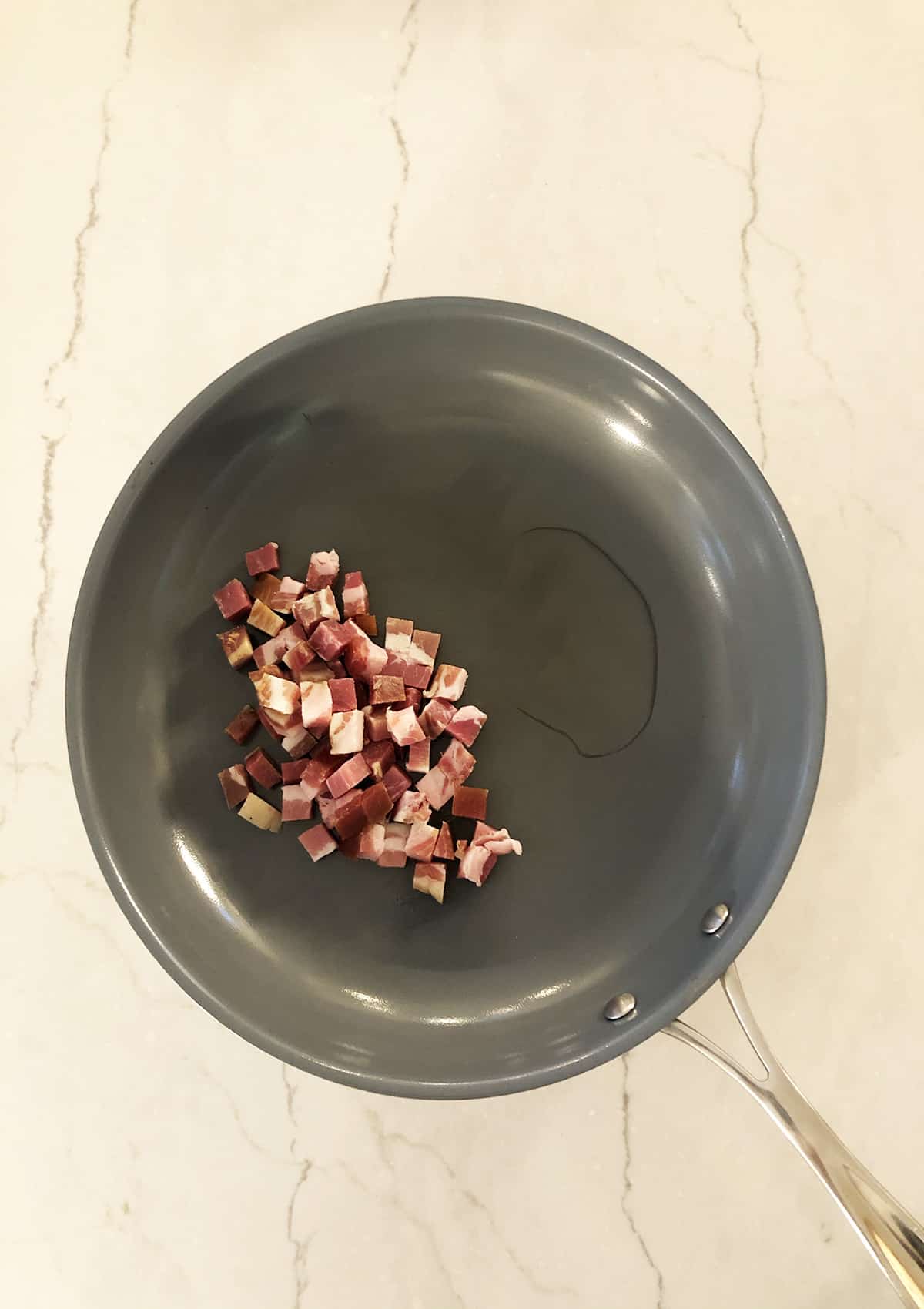 Pancetta cooking on a grey frying pan. 