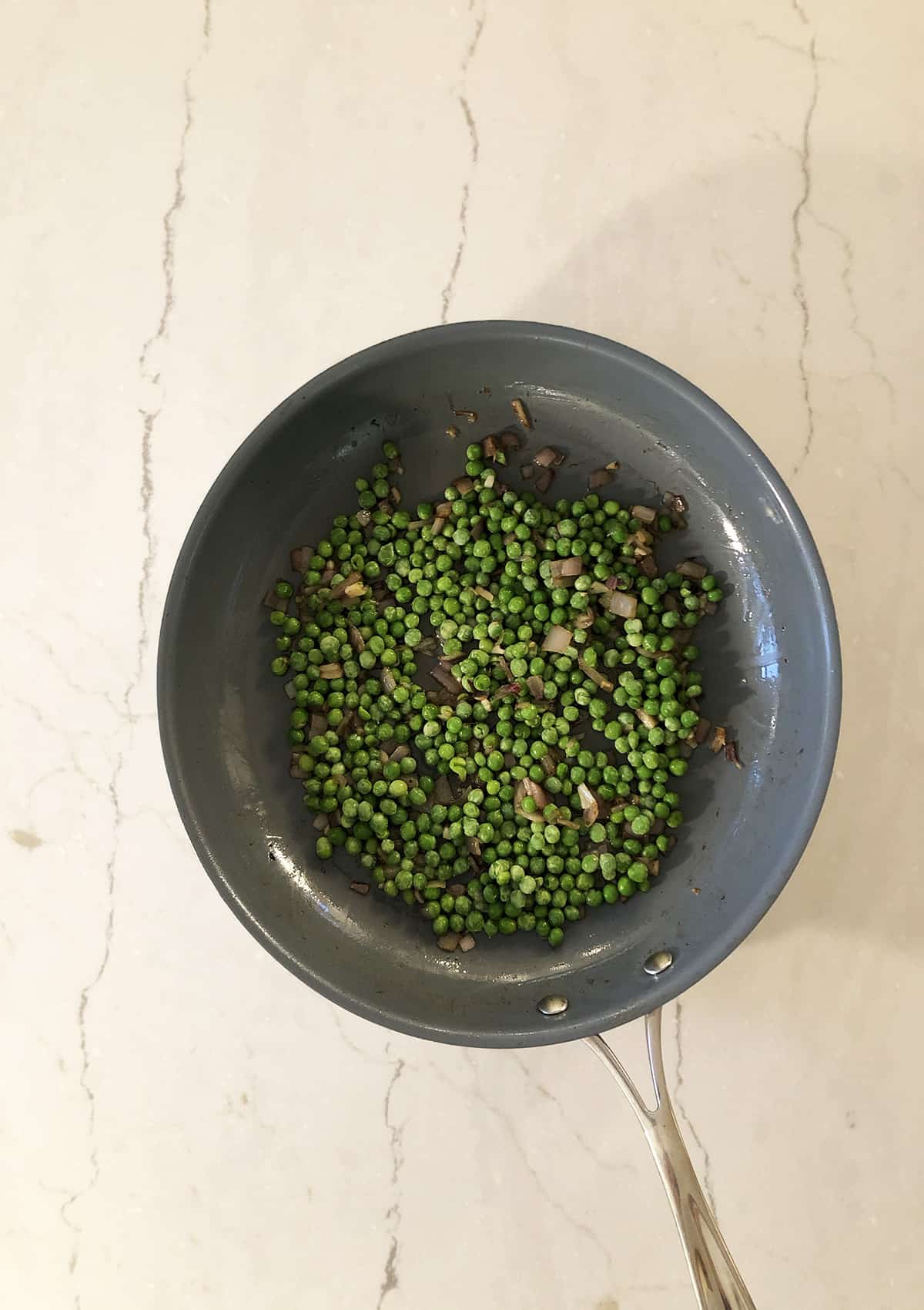 Frozen peas, shallots, and garlic in a gray frying pan. 