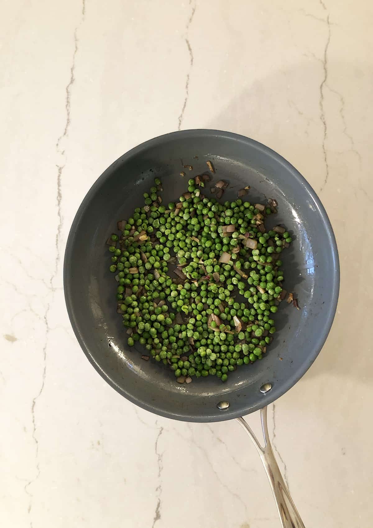 Frozen peas, shallots, and garlic in a gray frying pan.