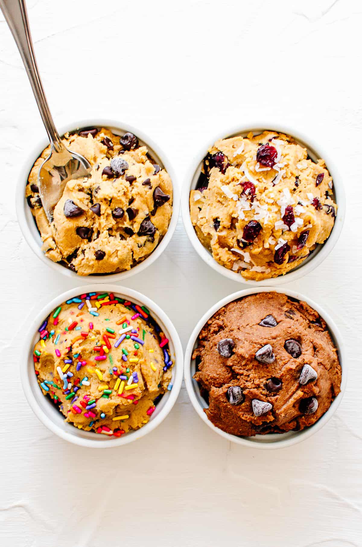 Birds eye view of four chickpea cookie dough flavour combinations in white bowls.