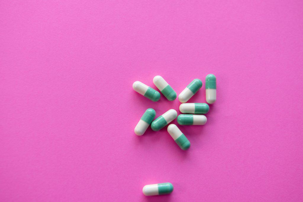 a variety of probiotic capsules against a pink background.