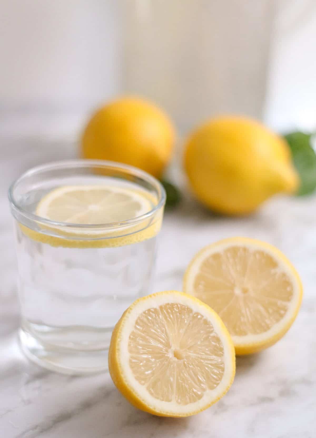 Lemon water with a sliced lemon and two halves of a lemon on the side. 