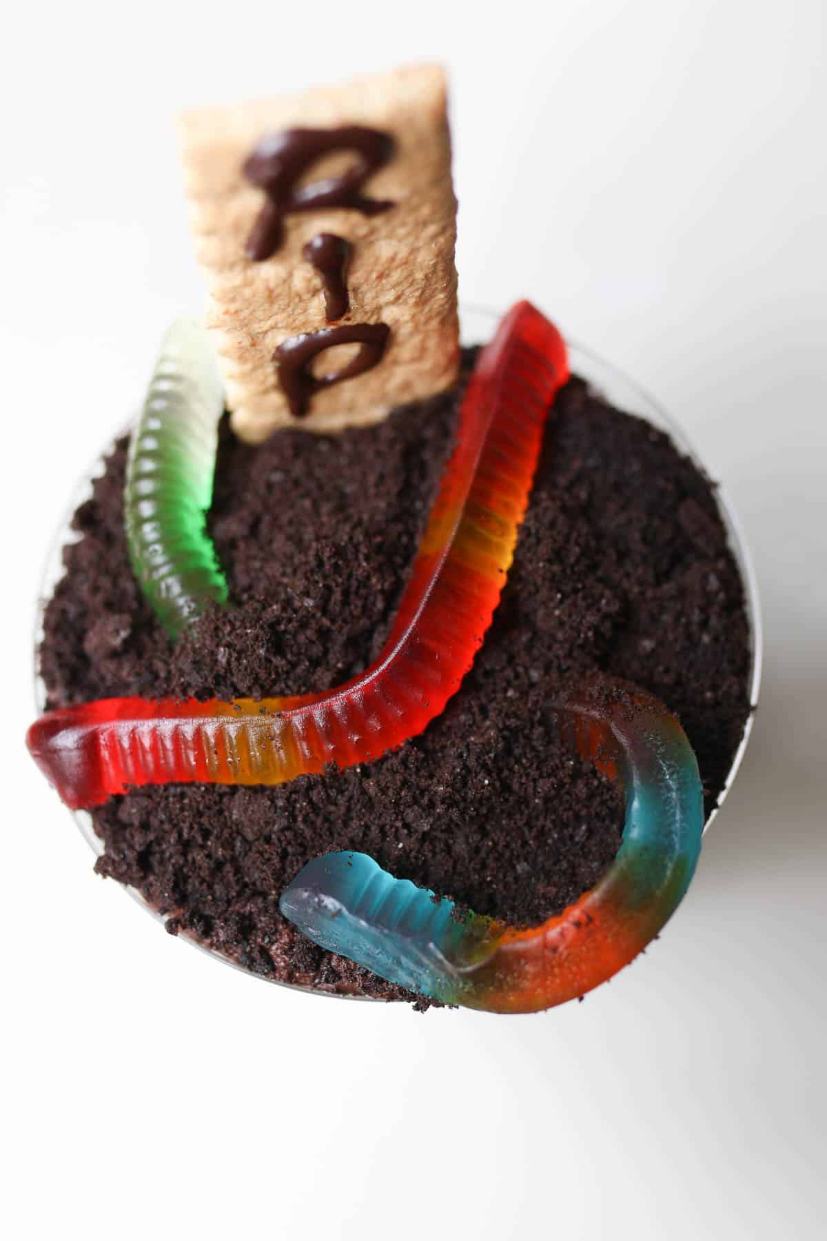 close up of halloween dirt cups with a graham cracker and gummy worms on top. 