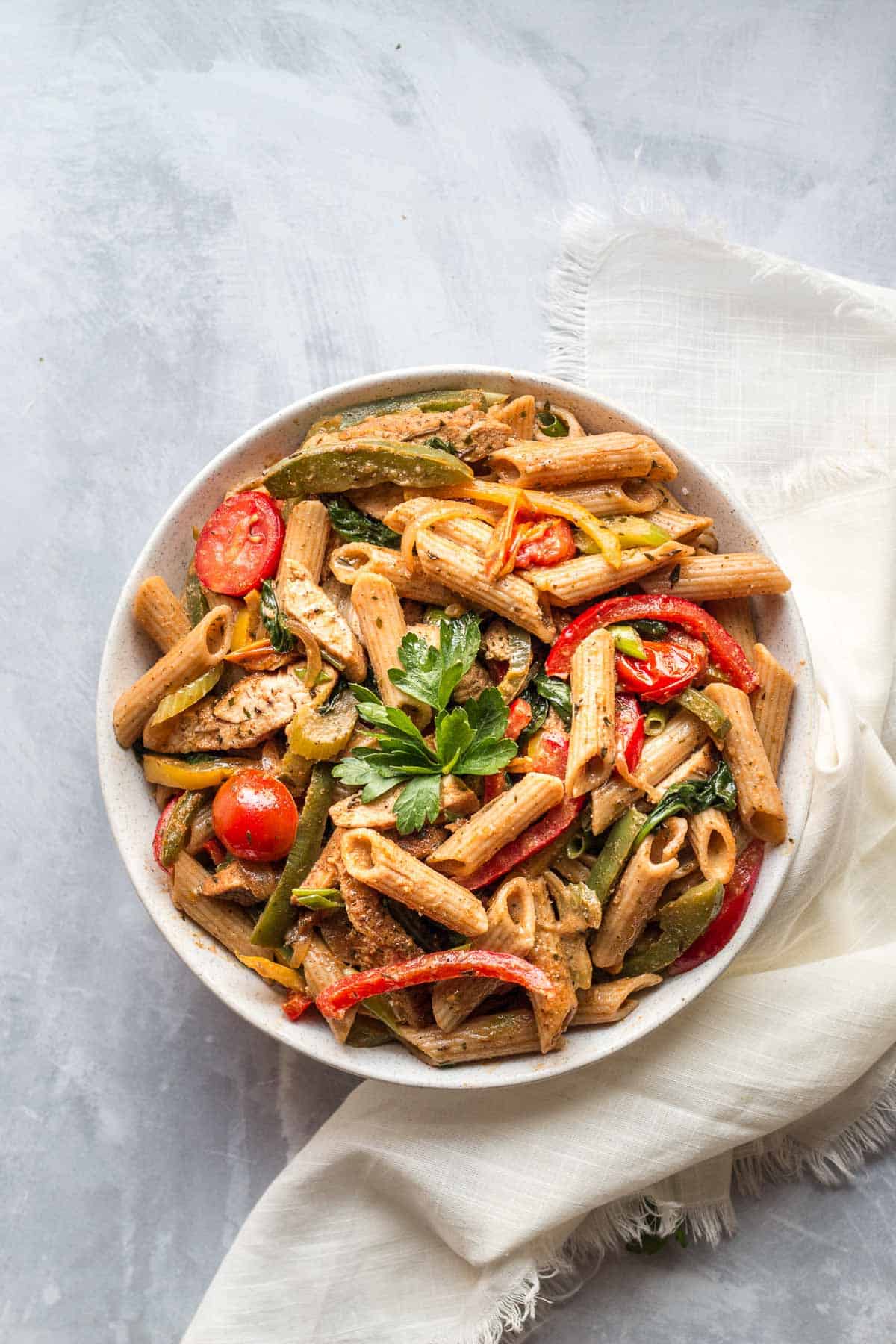 Birds eye view of jerk chicken pasta in a white bowl on top of a white cloth. 