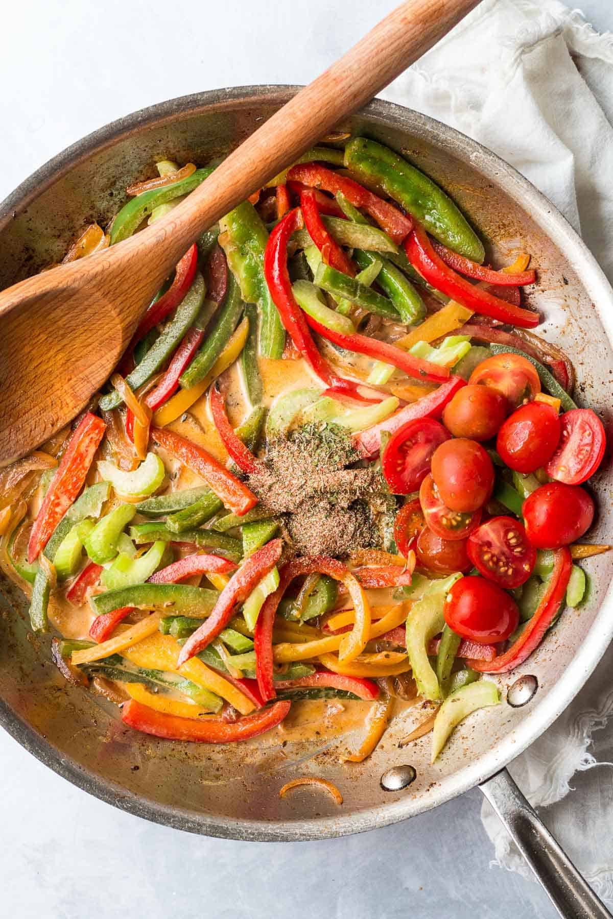 tomatoes and jerk seasoning added to frying pan with bell peppers and celery. 