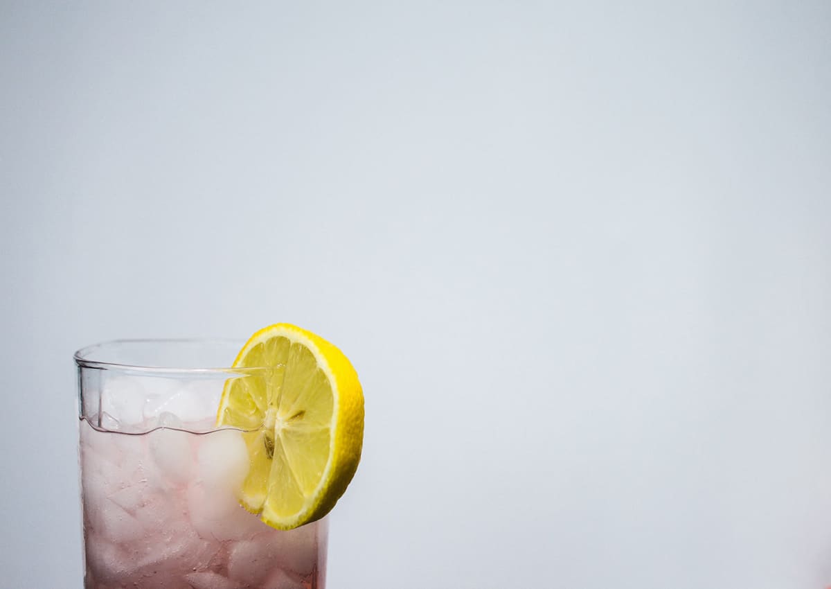 A beverage with ice and a lemon wedge on the rim. 