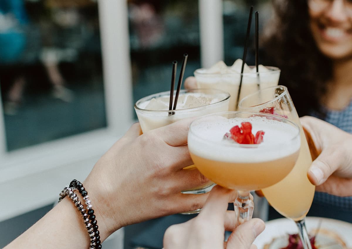 Four people "cheersing" their alcoholic beverages. 