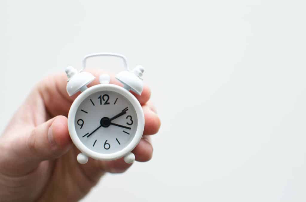 Hand holding up a small white alarm clock.