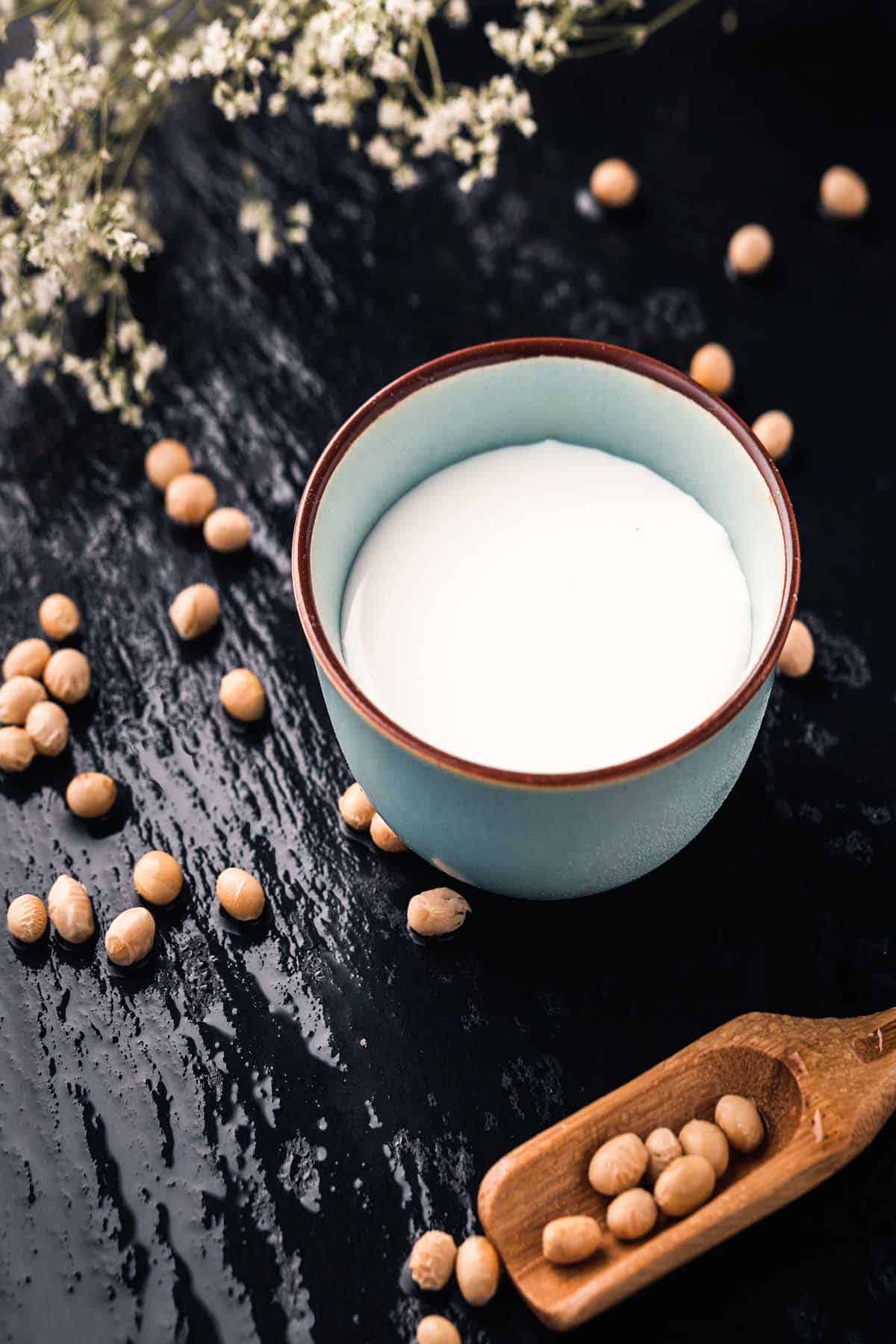 Soy milk in a blue mug with soy beans surrounding. 