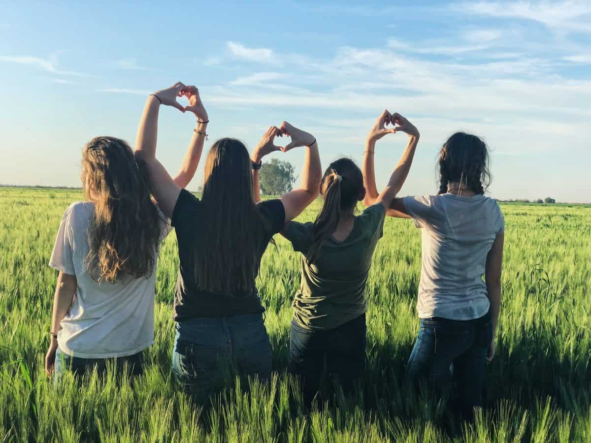 Several teen girls standing in a field making heart signs with their hands.