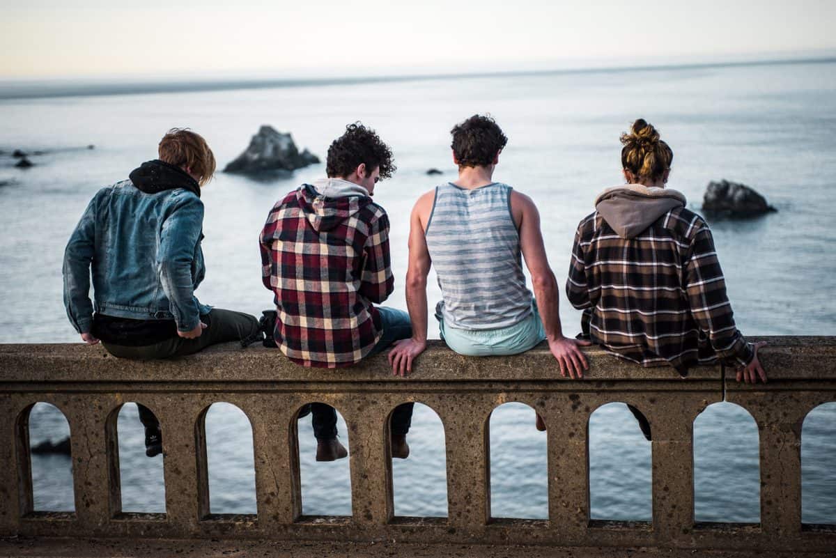 Several teens sitting together on a bridge.