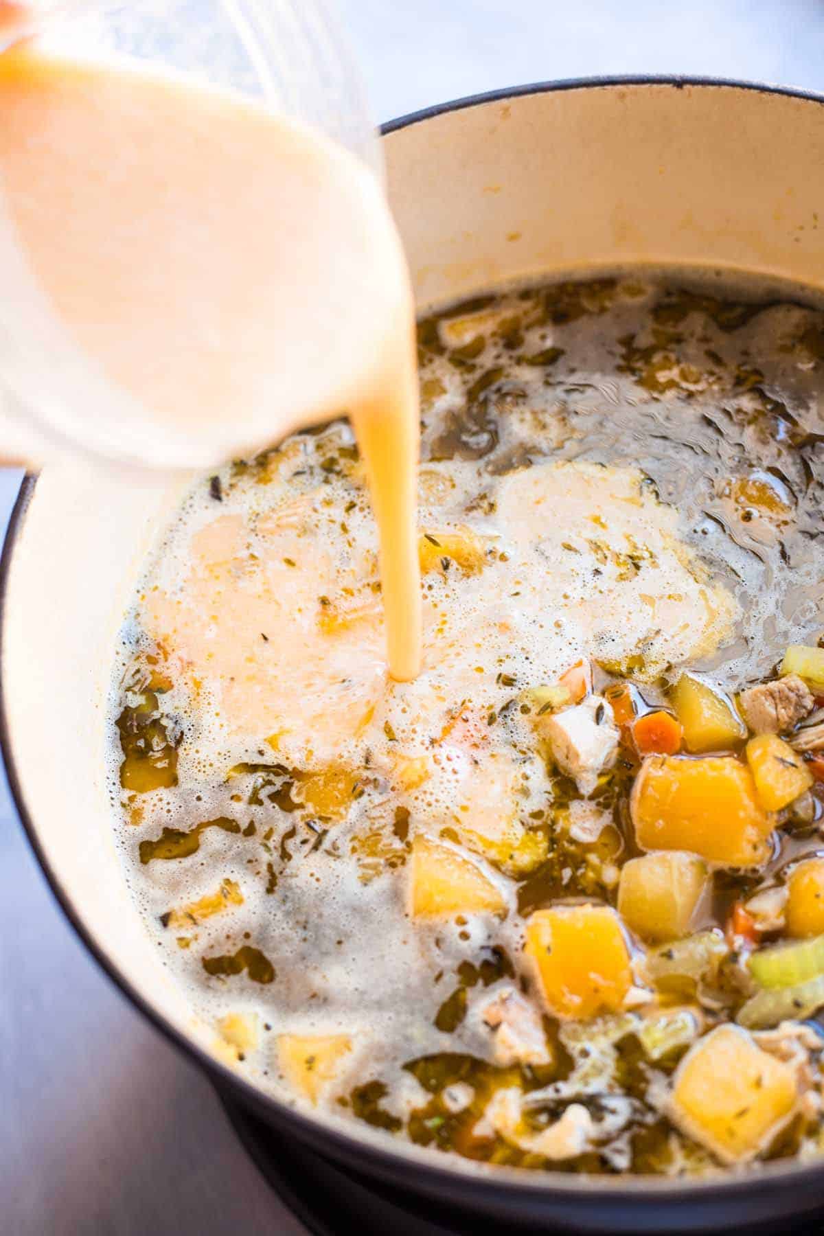 Blended butternut squash and cannelini beans being poured into turkey soup.