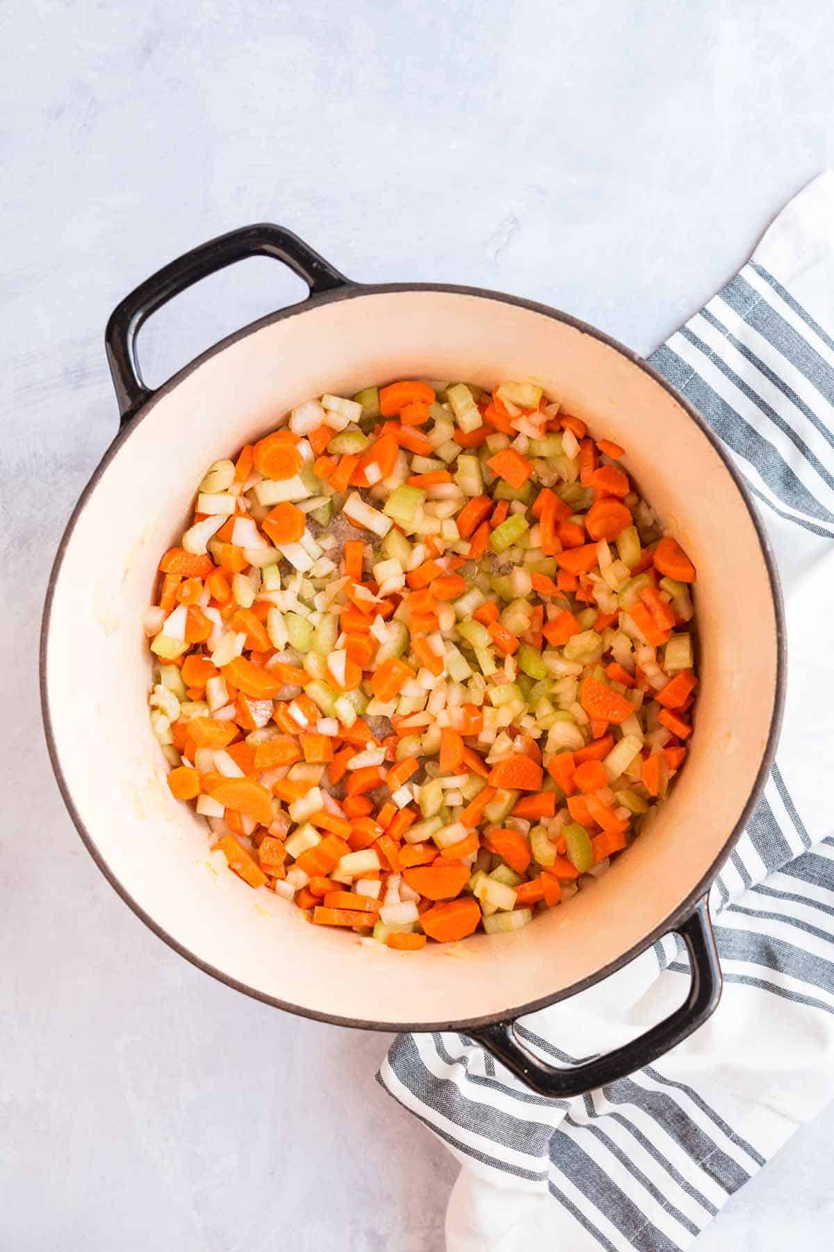 Chopping carrots, celery, and onion cooking in a sauce pot.