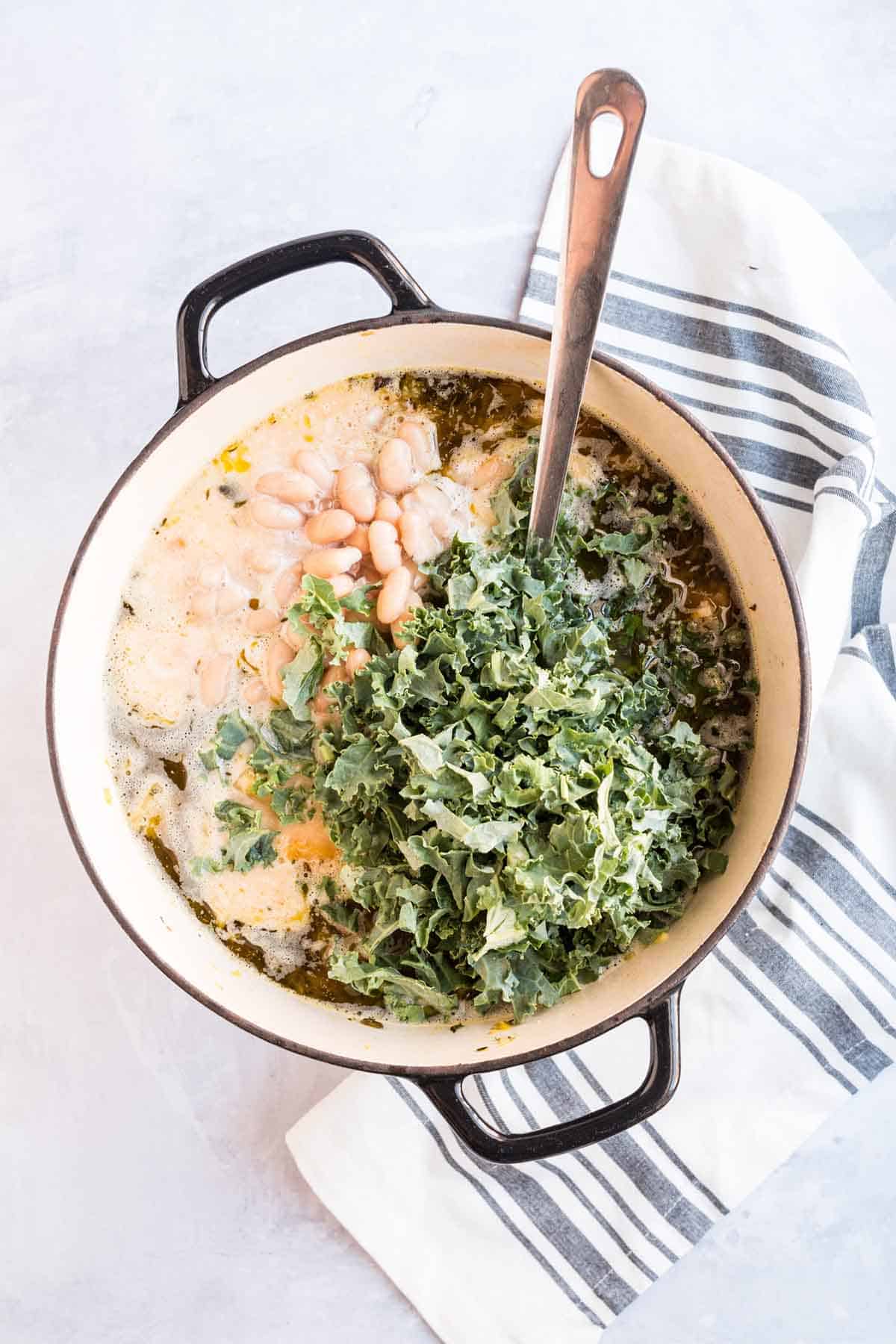 Chopped kale and white beans added to leftover turkey soup cooking in sauce pot.