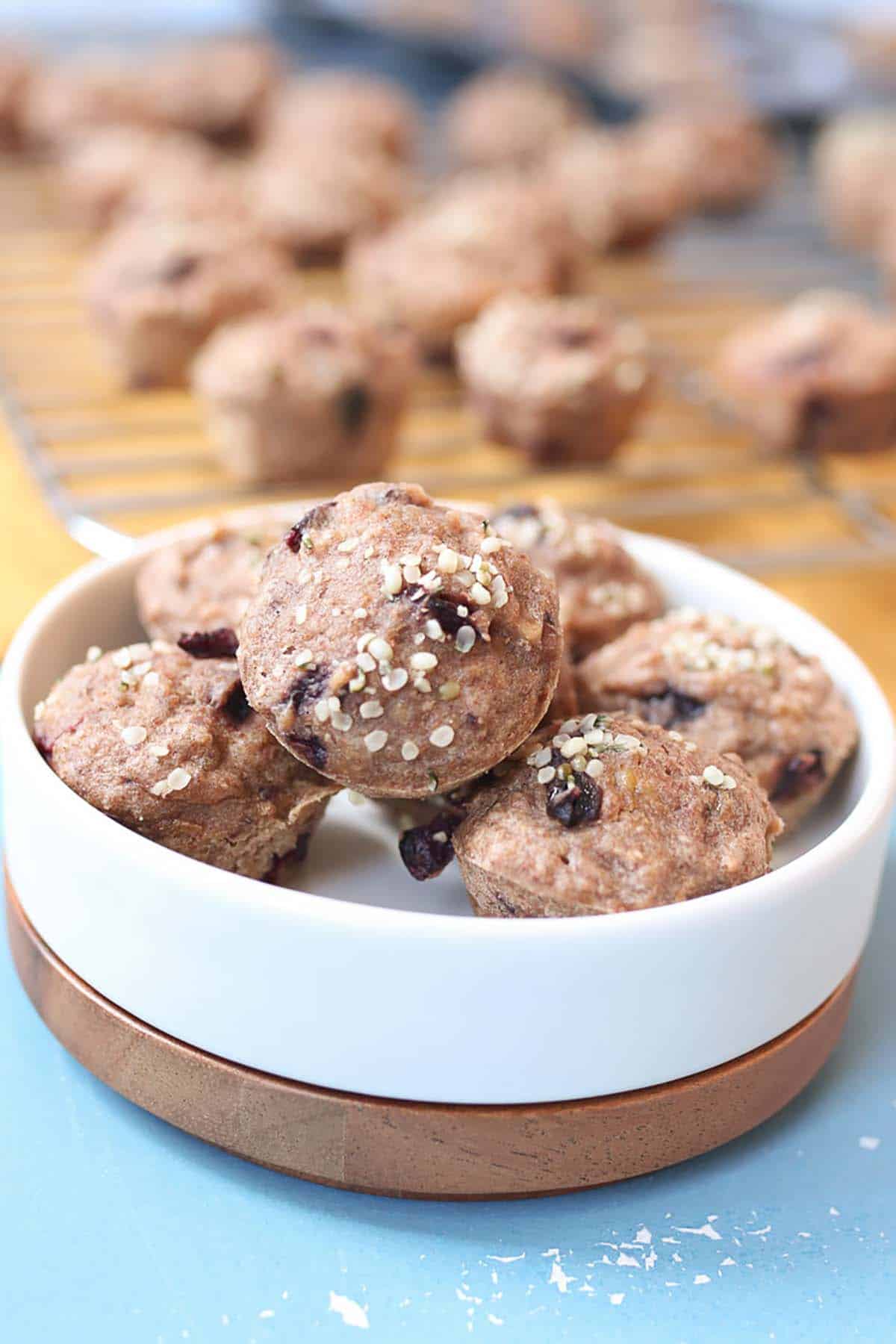 Several mini banana muffins on a white plate with ore muffins on a muffin tray in the background.