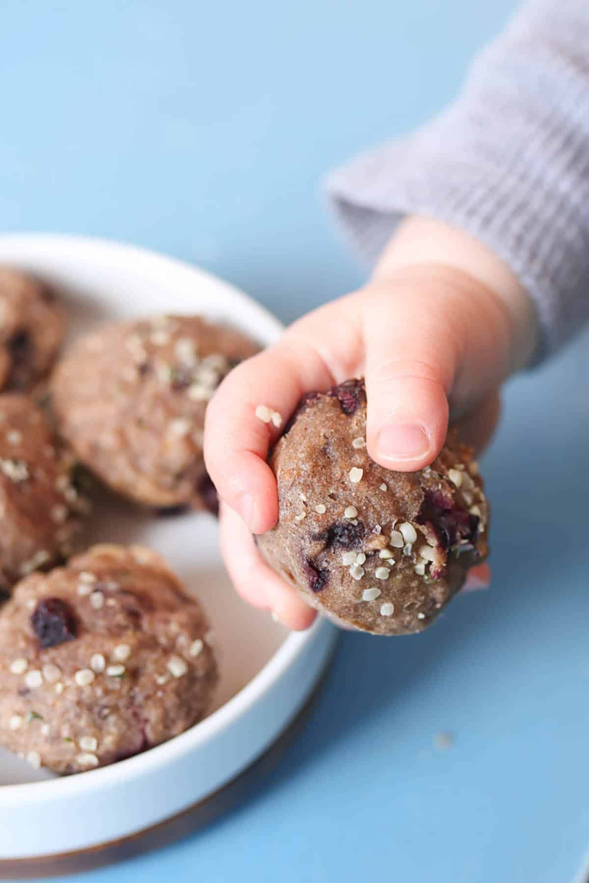 A baby hand reaching for banana mini muffins on a plate. 