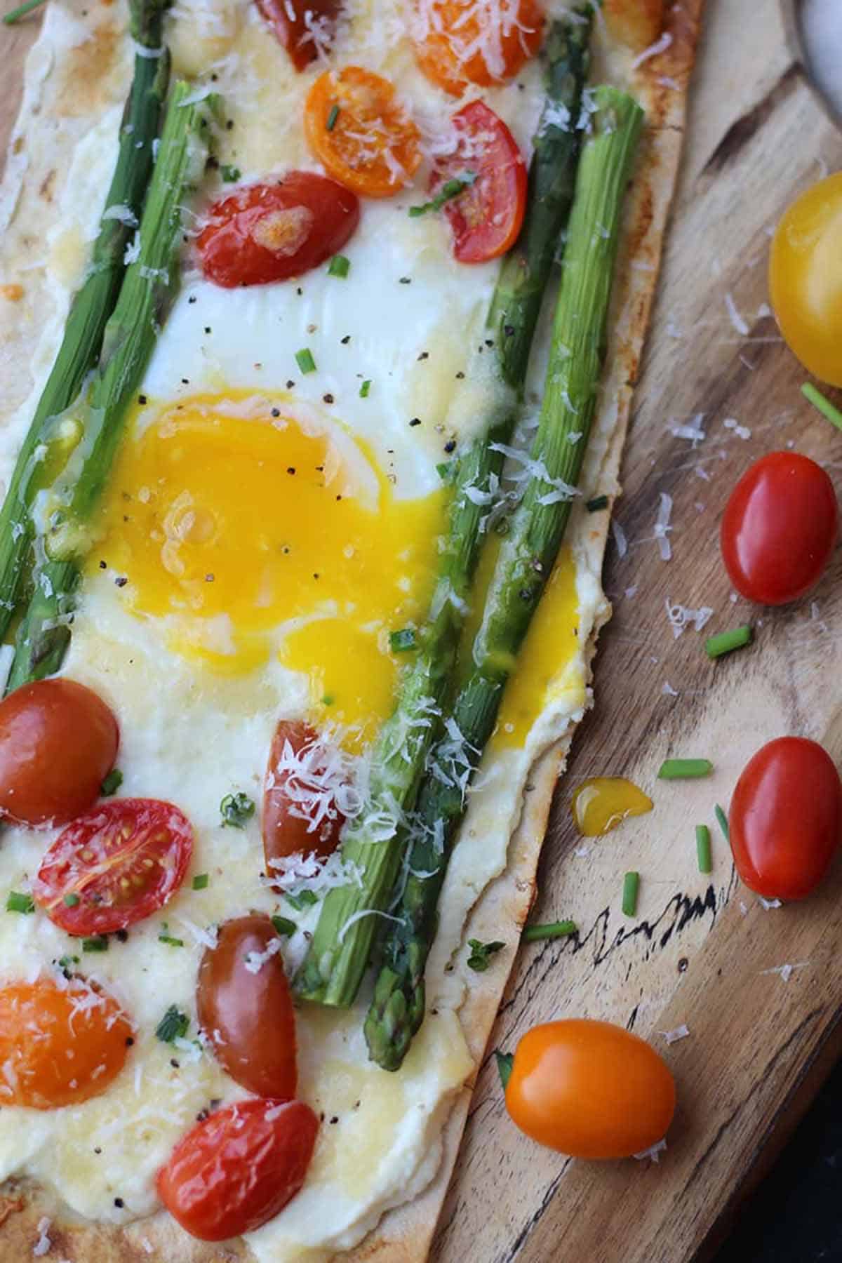 A breakfast pizza on a wooden board with cherry tomatoes on the side. 