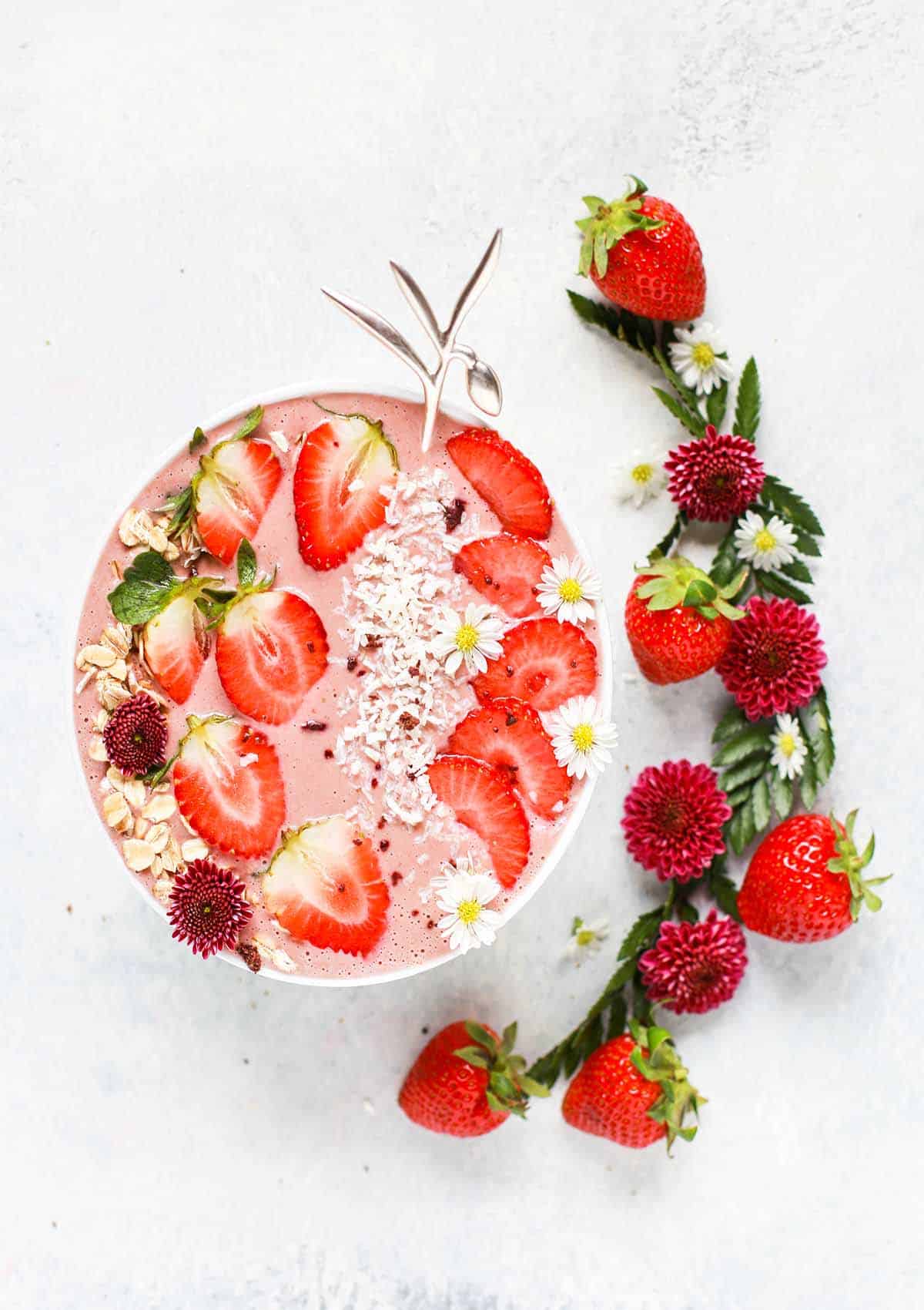 A pink smoothie bowl topped with strawberries, coconut flakes, and oatmeal. 