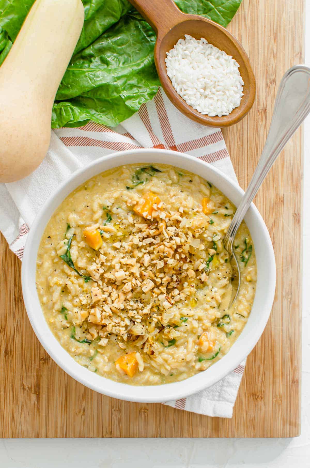 Birds eye view of butternut squash risotto in a white bowl on a wooden board with rice and butternut squash in the background.