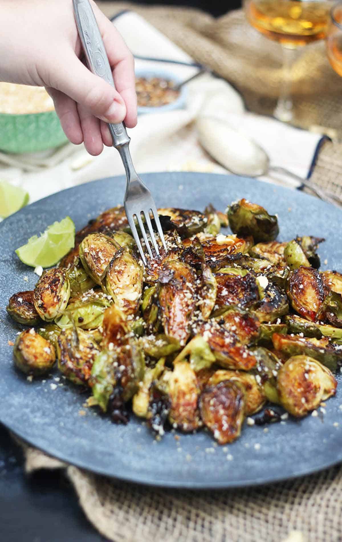 Hand with a fork digging into sweet and spicy Brussel sprouts on a plate. 