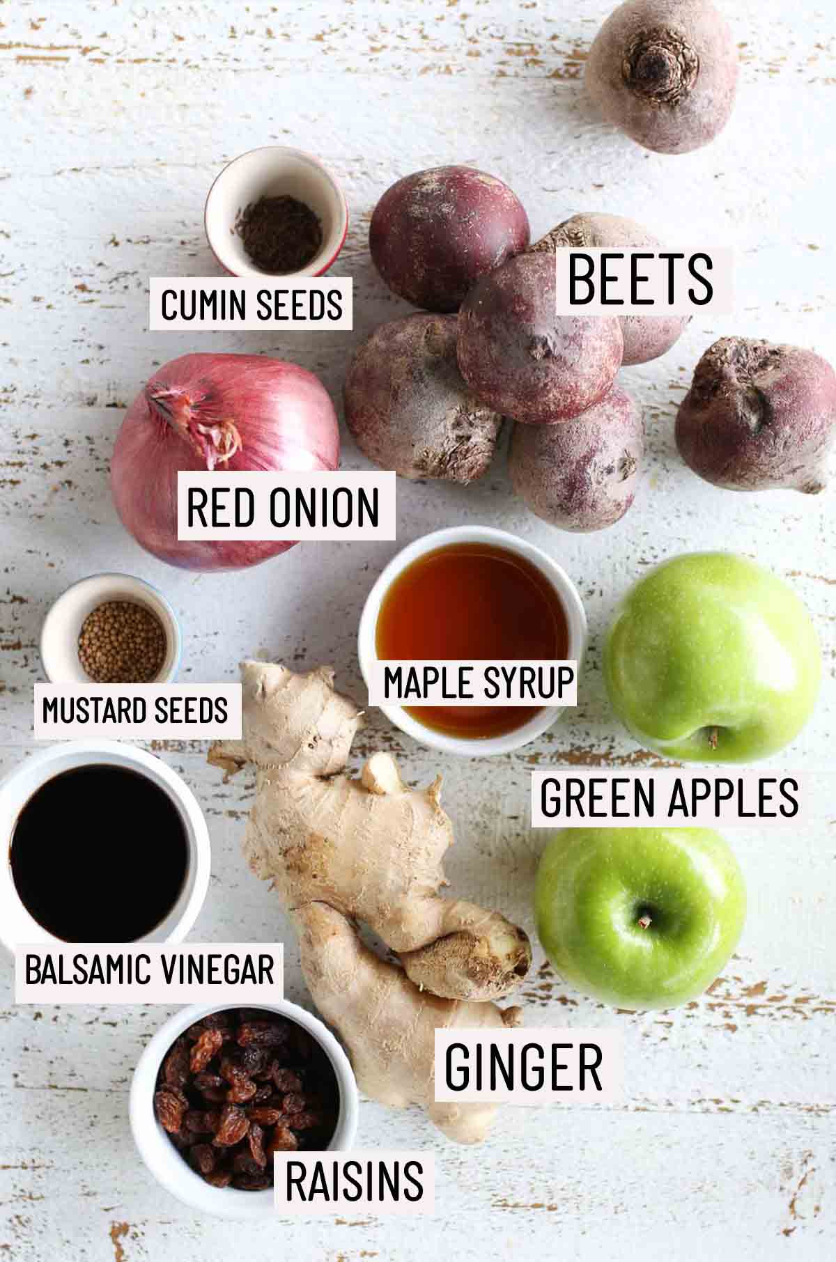 Birds eye view of portioned ingredients needed to make apple chutney including beets, red onion, cumin seeds, mustard seeds, maple syrup, green apples, ginger, balsamic vinegar, and raisins. 