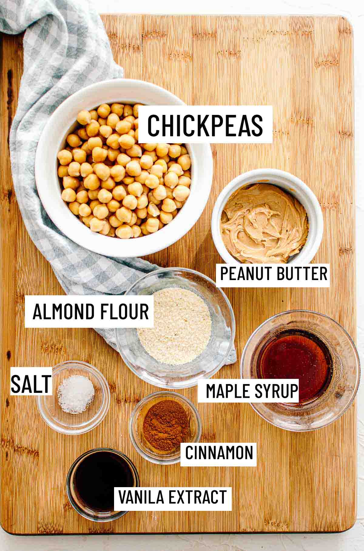 Birds eye view of portioned chickpea cookies dough ingredients including chickpeas, peanut butter, almond flour, maple syrup, salt, vanilla extract, and cinnamon. 