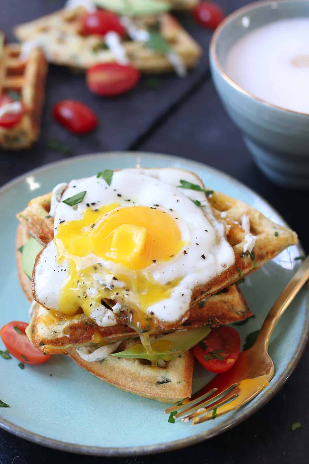 A fried egg on top of three waffles sitting on a blue plate with a fork on the side. 