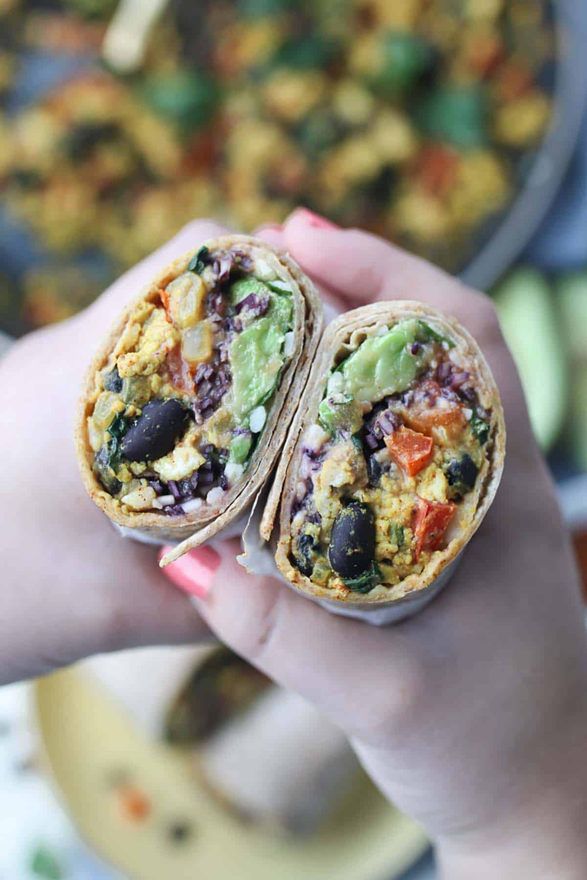 A person holding up a breakfast burrito with eggs. 