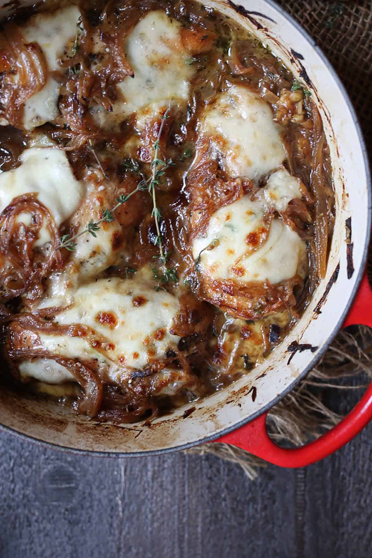 Birds eye view of French onion chicken breast in a red pot topped with thyme. 