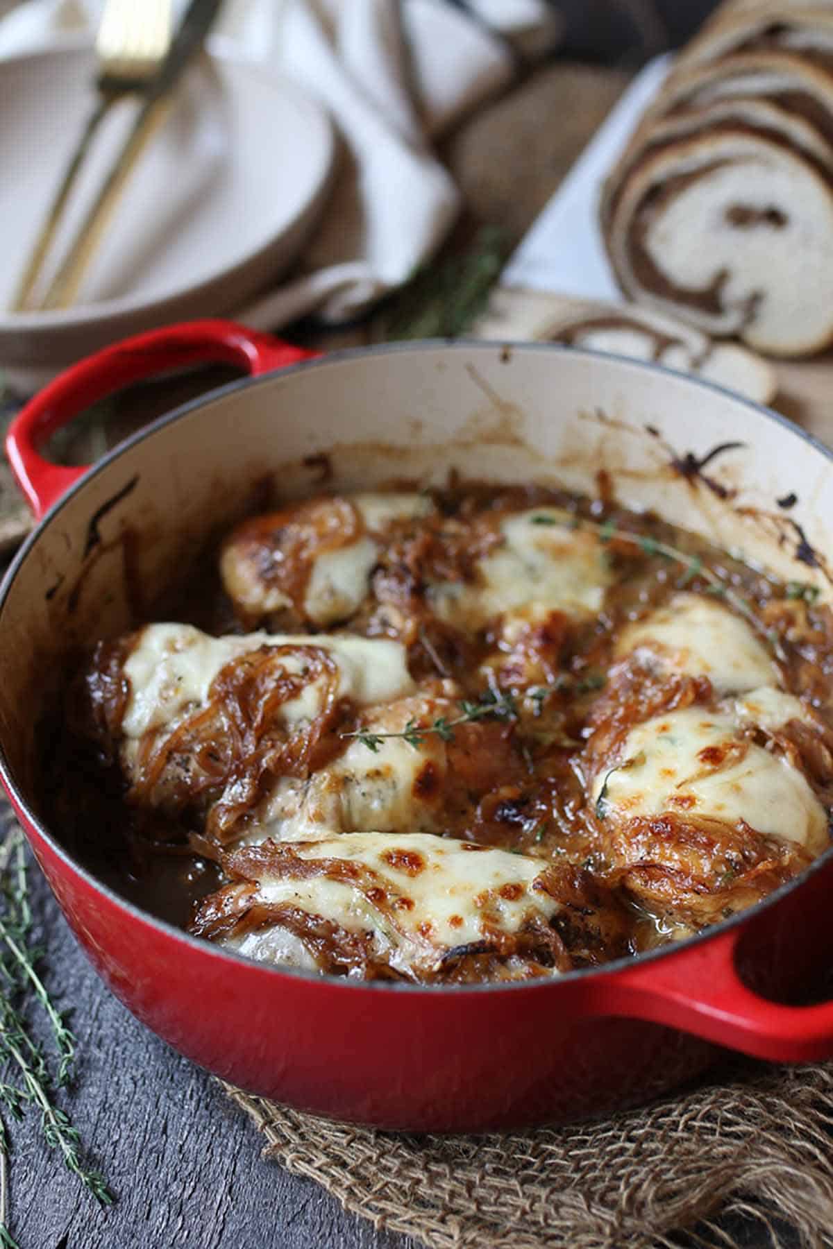 French onion chicken breast in a red pot garnished with a thyme sprig. 