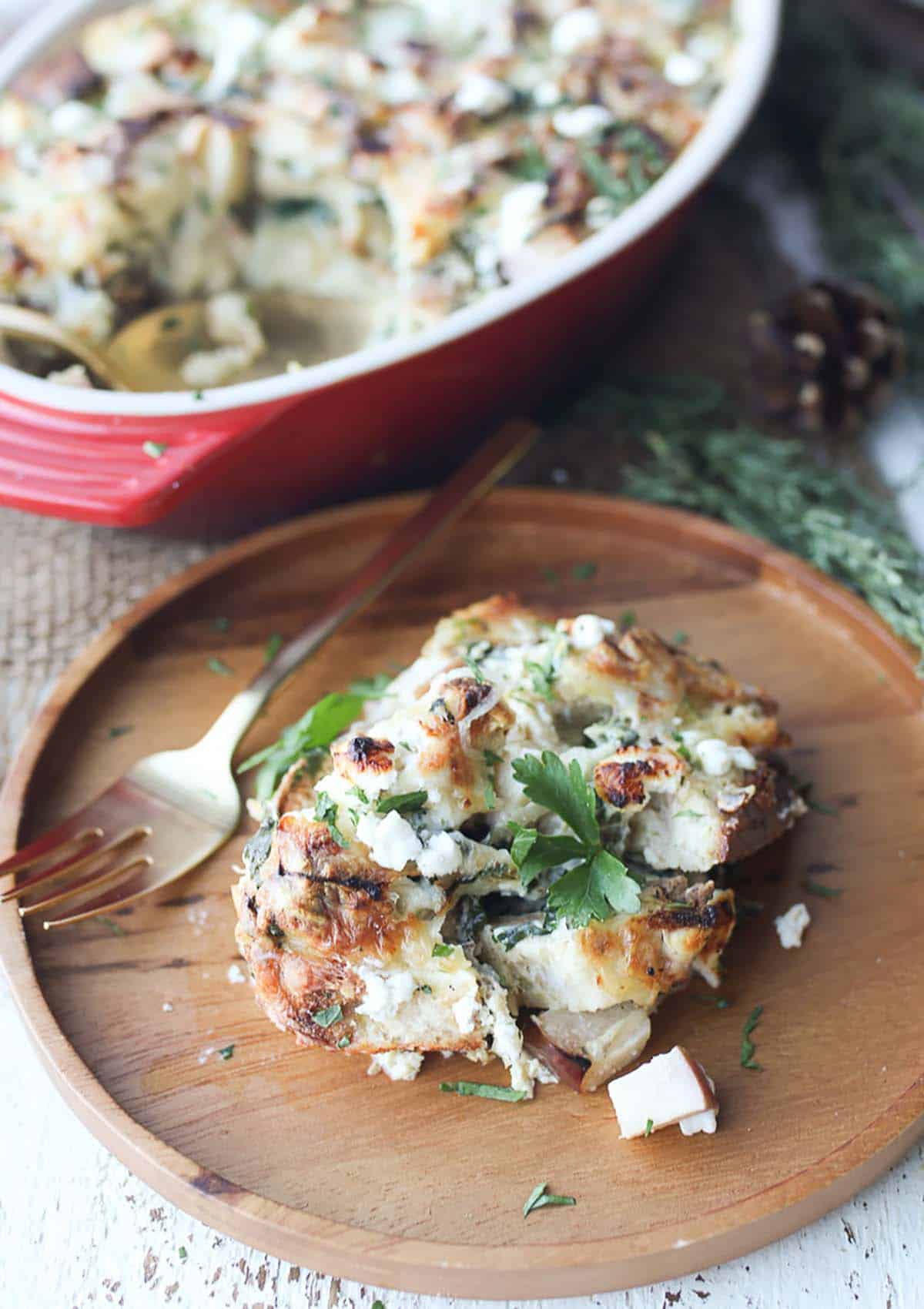 A serving of vegetarian strata on a brown wooden plate with a fork on the side, topped with parsley. 