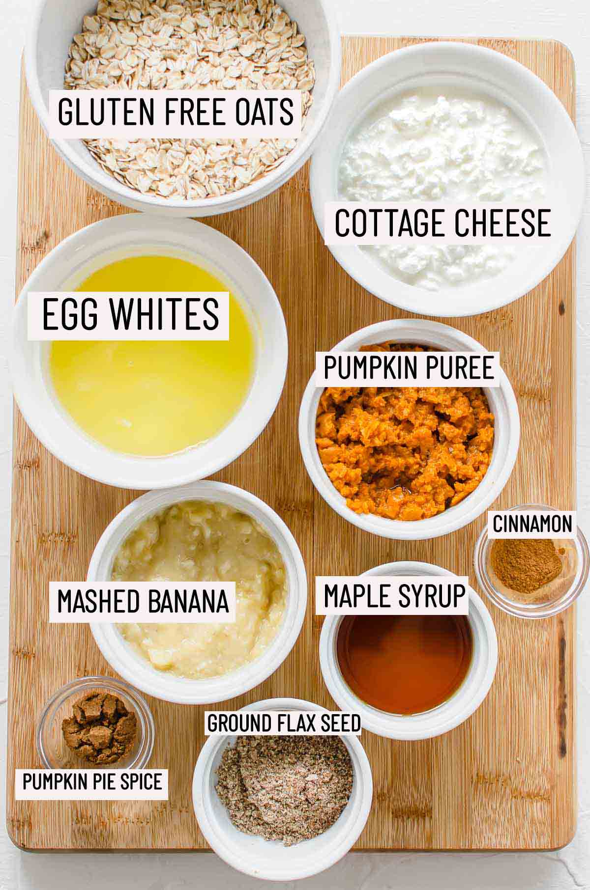 Portioned ingredients for protein pumpkin pancakes including oats, cottage cheese, egg whites, pumpkin puree, cinnamon, mashed banana, maple syrup, flax seed, and pumpkin pie spice.