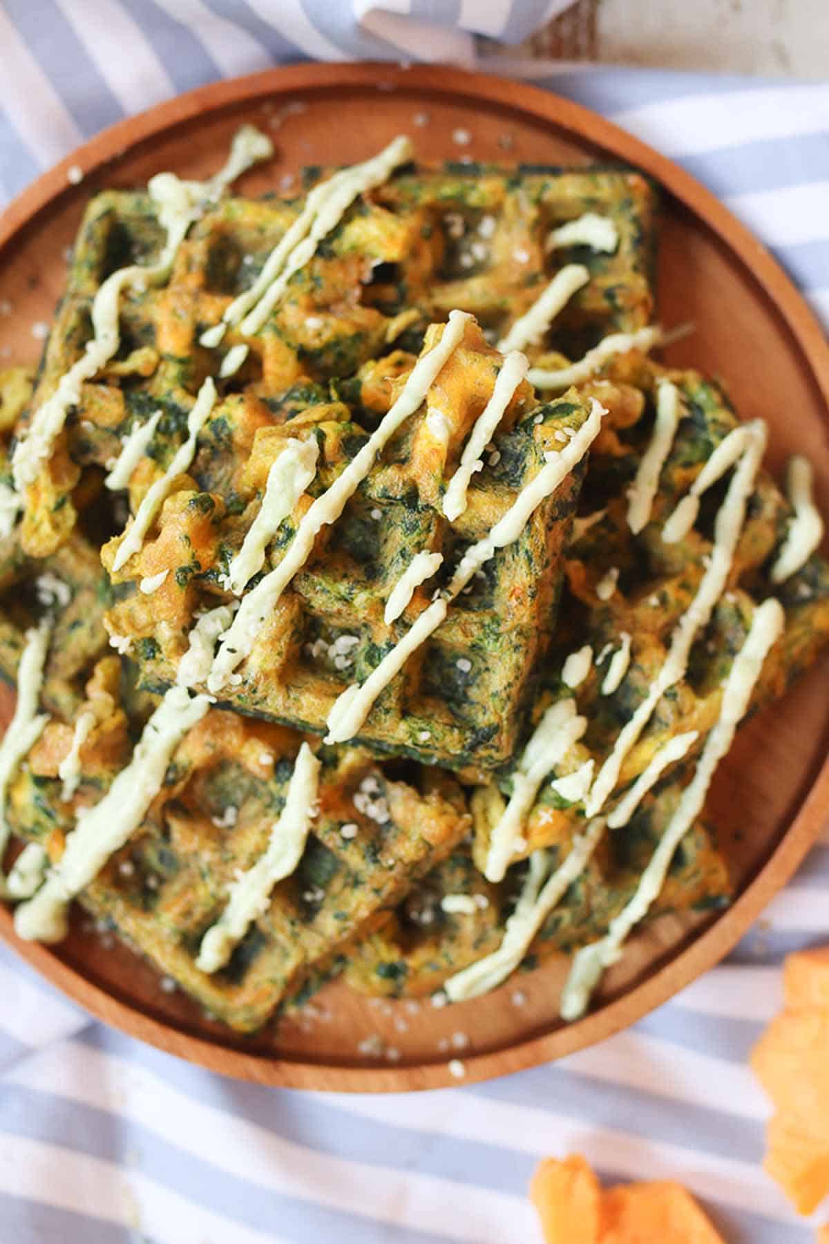 Several savory waffles on a wooden plate drizzled with white sauce.