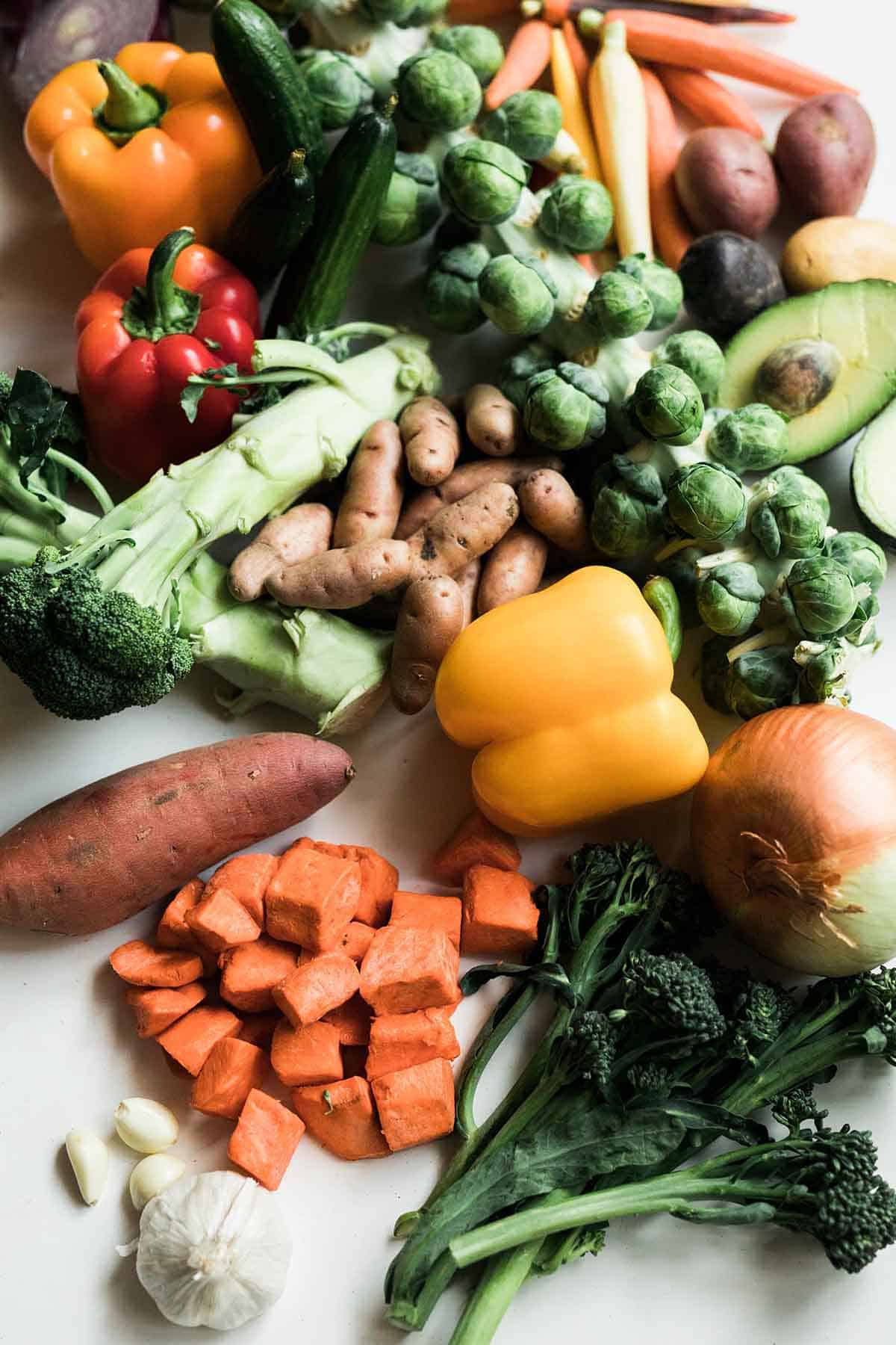 A large spread of colourful vegetables from a vegan grocery list including sweet potato, bell peppers, onion, broccoli, brussel sprouts, carrots, avocado, and zucchini.