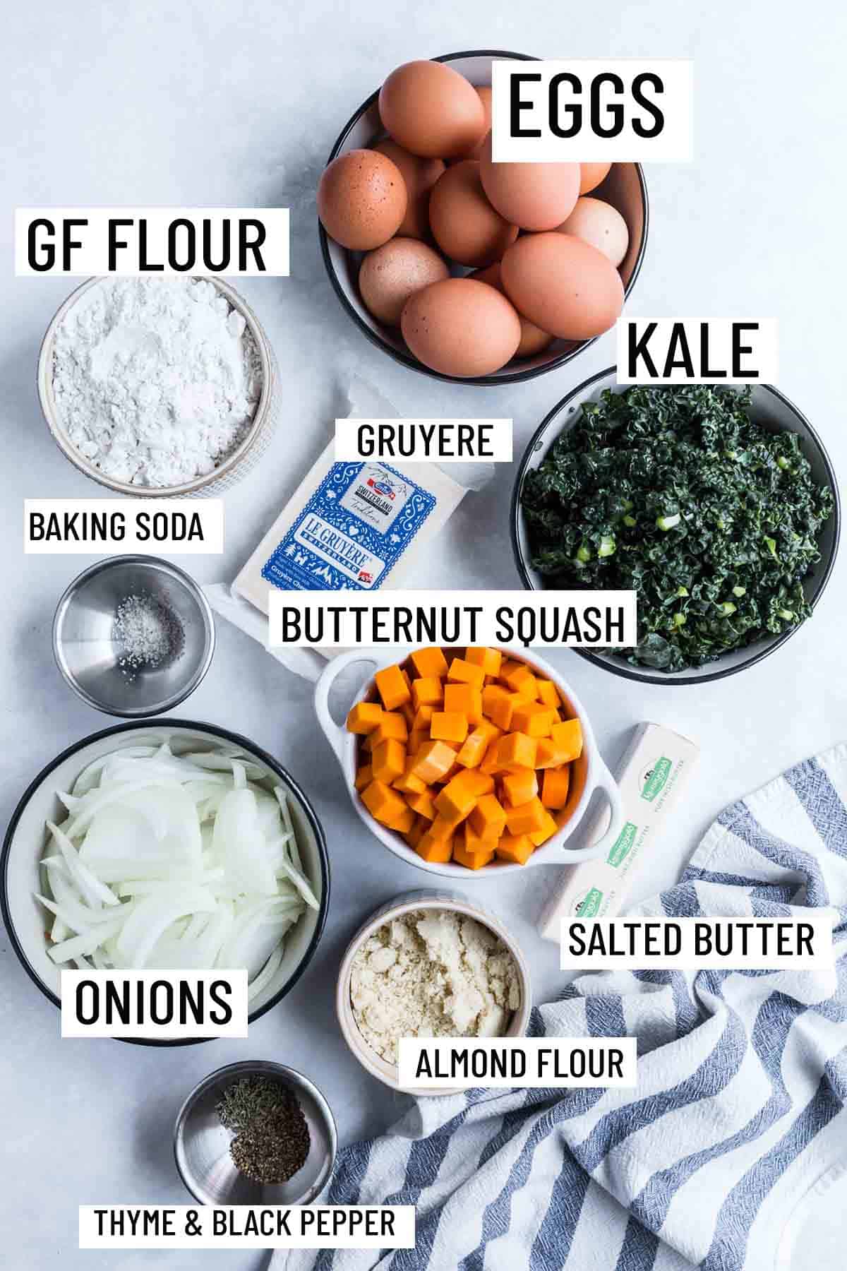 Birds eye view of portioned ingredients to make gluten free quiche including butternut squash, kale, almond flour, salted butter, onions, gruyere, gluten free flour, and eggs. 