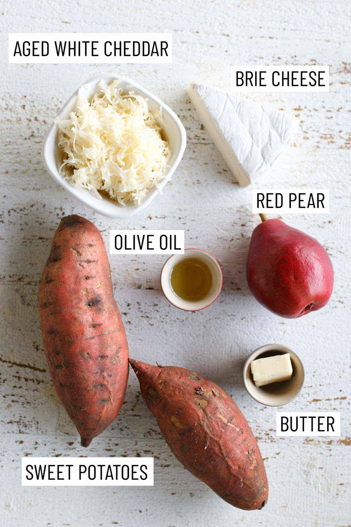 Overhead image of ingredients needed to make the recipe: sweet potatoes, aged white cheddar, bri cheese, olive oil, red pear, and butter.