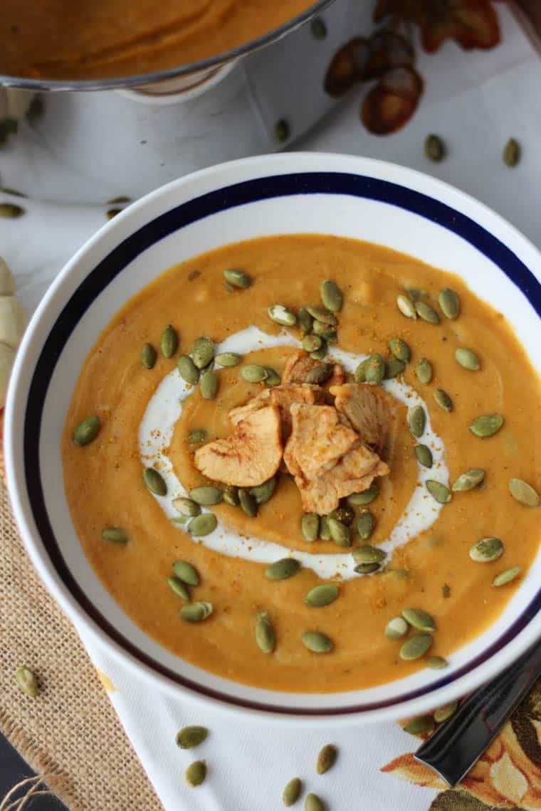 Overhead over of a bowl of sweet potato curry soup with coconut milk drizzled over with pumpkin seeds and baked apple chips sprinkled on top.