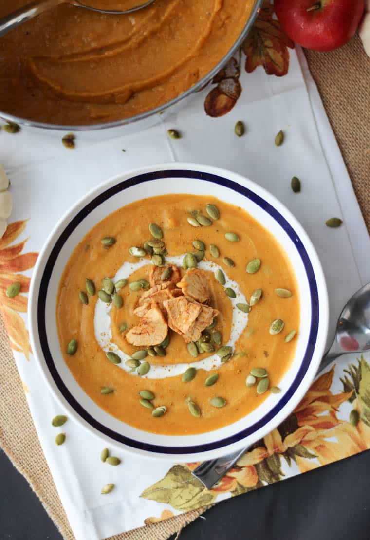 Overhead over of a bowl of sweet potato curry soup with coconut milk drizzled over with pumpkin seeds and baked apple chips sprinkled on top.