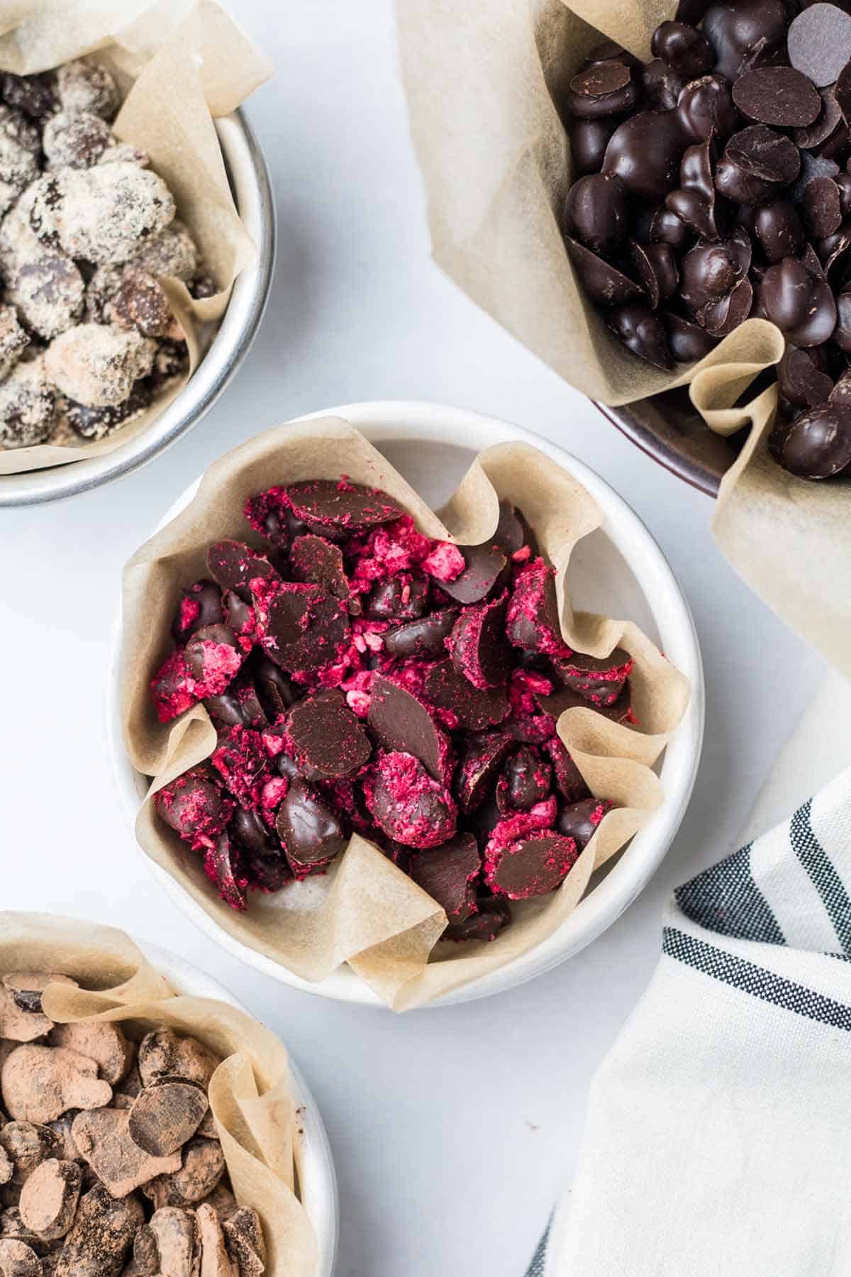 Multiple small parchment lined bowls of chocolate covered espresso beans with each bowl containing different toppings.