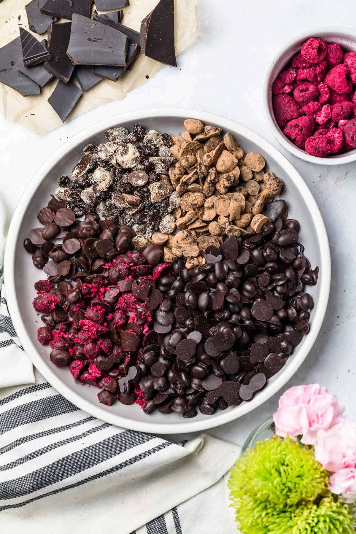 A white plate containing multiple chocolate covered espresso beans with a variety of toppings such as crushed berries and cacao powder. 