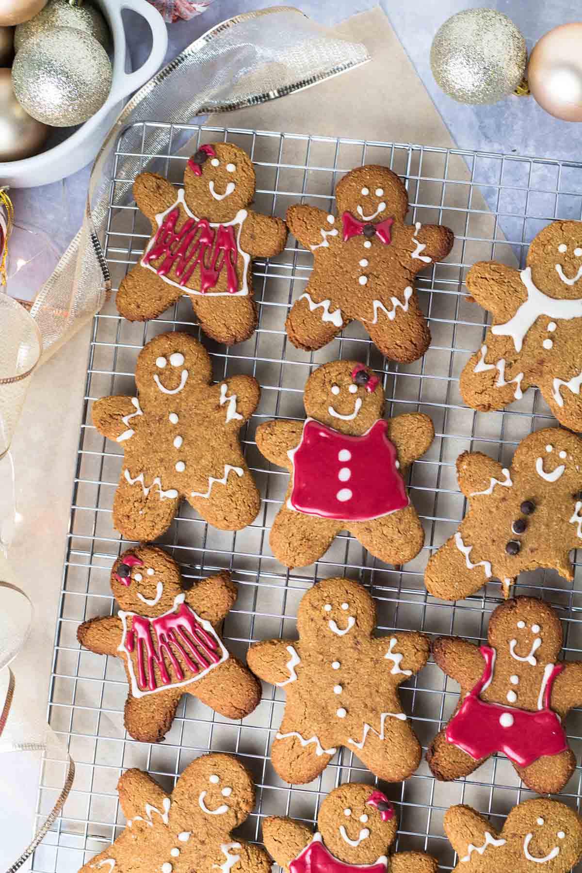 Birds eye view of several gingerbread cookies on a cooling rack surrounded by Christmas ornaments. 