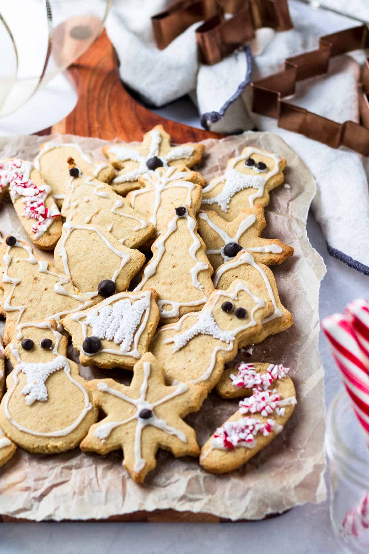 Several gluten free Christmas cookies sitting on parchment paper with Christmas cookie cutters and candy canes in the background. 