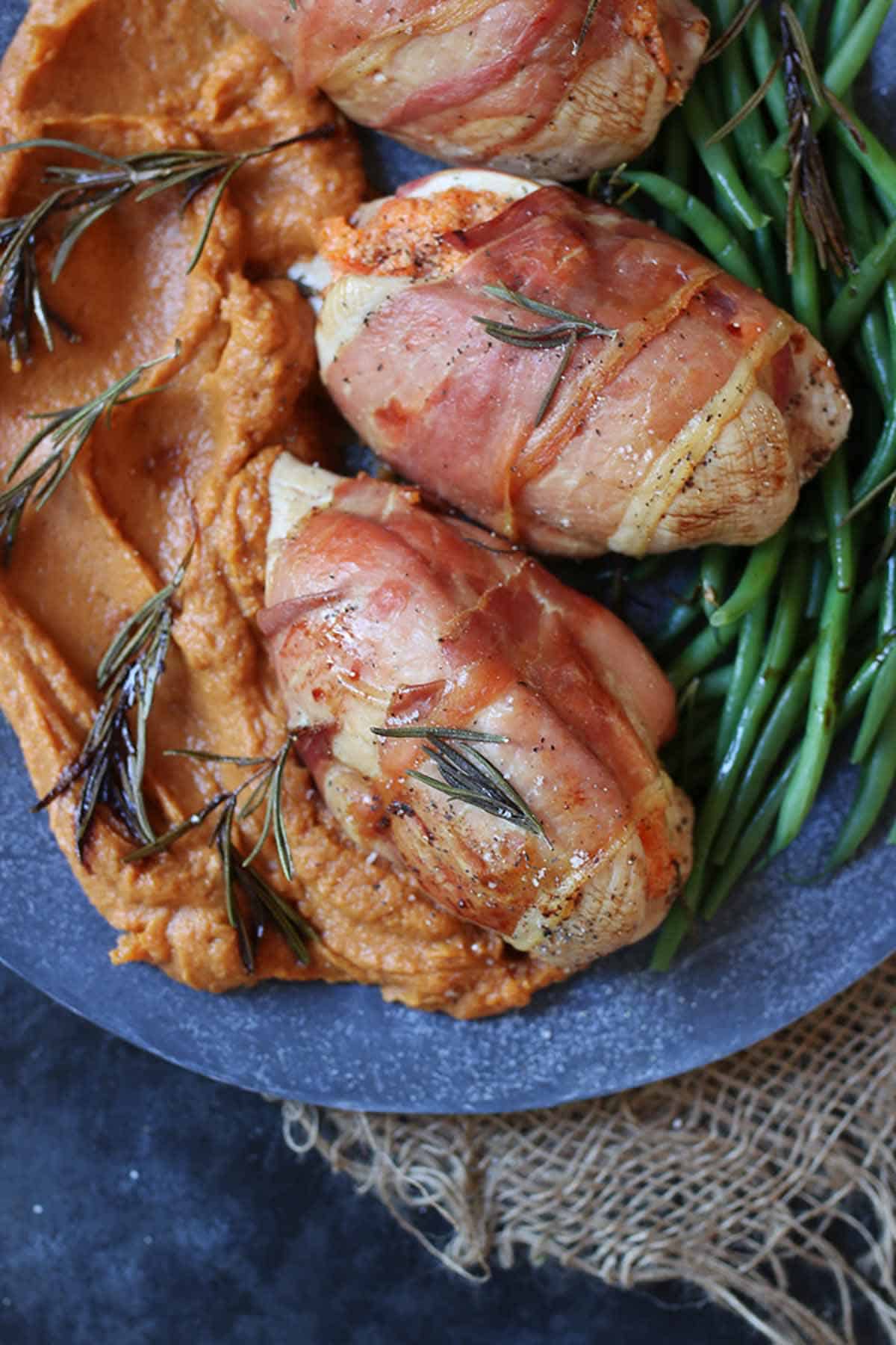 Close up of stuffed chicken breasts  on a plate with mashed sweet potato and green beans on the side. 