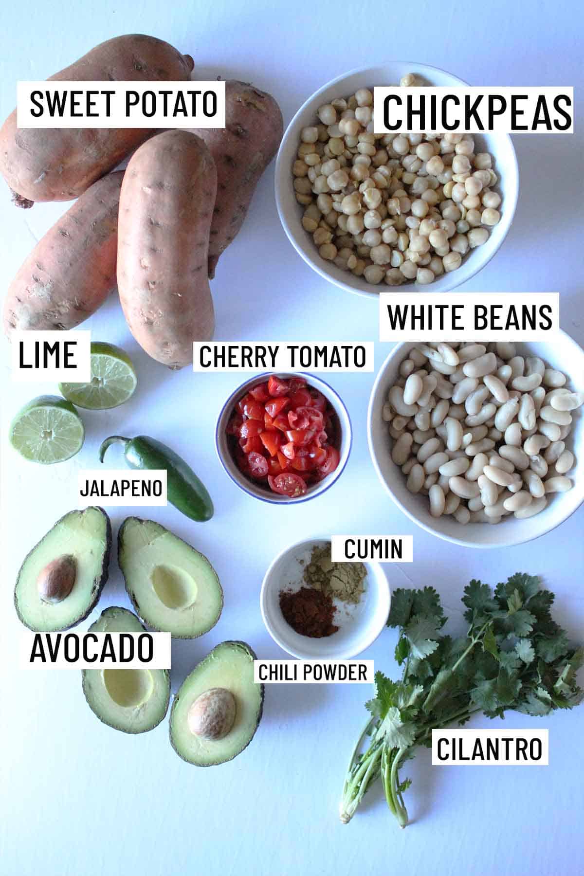 Birds eye view or portioned ingredients for guacamole stuffed sweet potatoes including sweet potato, avocado, cilantro, chili powder, cumin, white beans, cherry tomato, chickpeas, lime, and cilantro. 