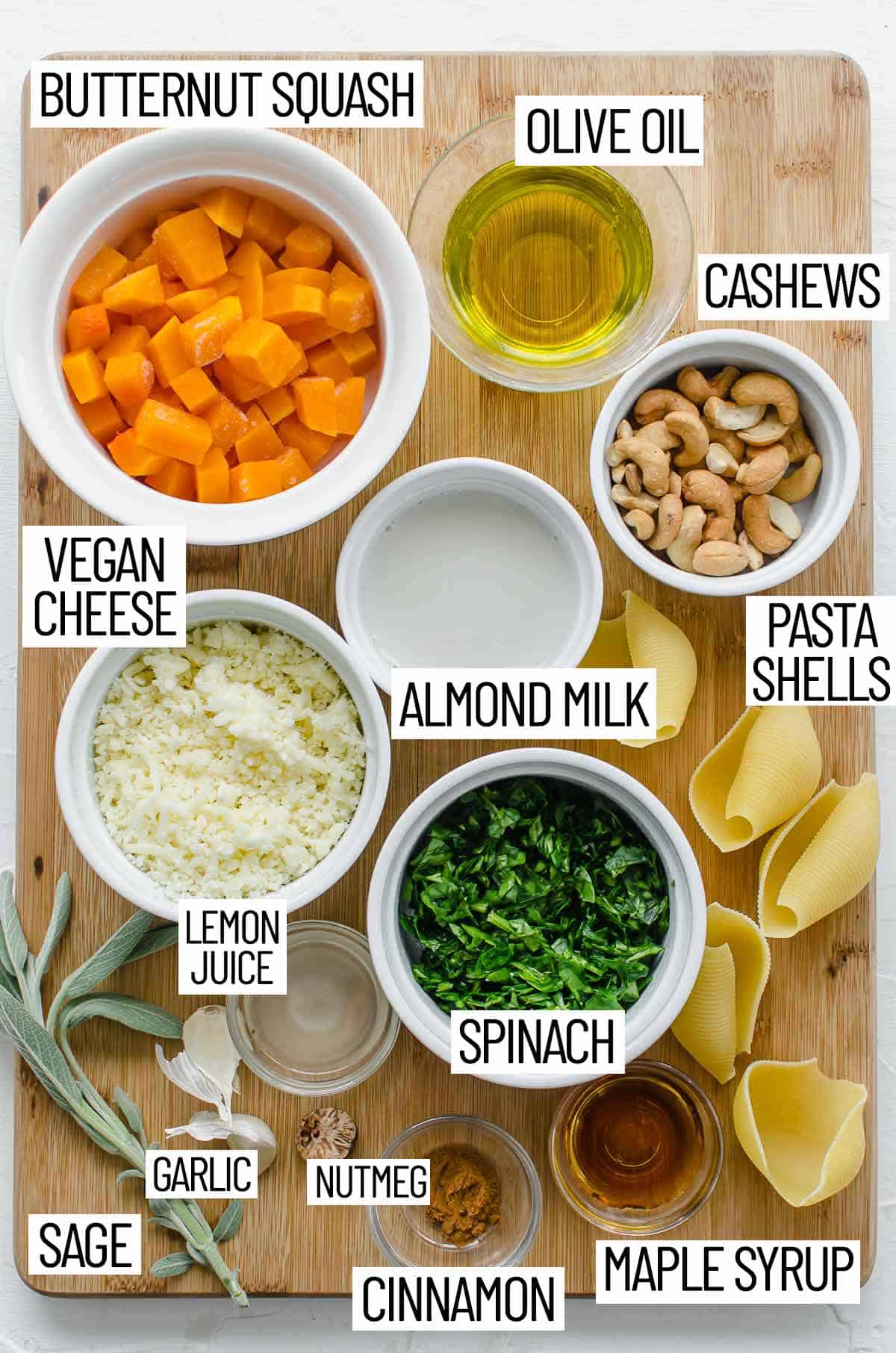 Overhead image of ingredients for stuffed shells including butternut squash, olive oil, cashews, pasta shells, almond milk, vegan cheese, lemon juice, spinach, maple syrup, cinnamon, nutmeg, garlic, and sage.