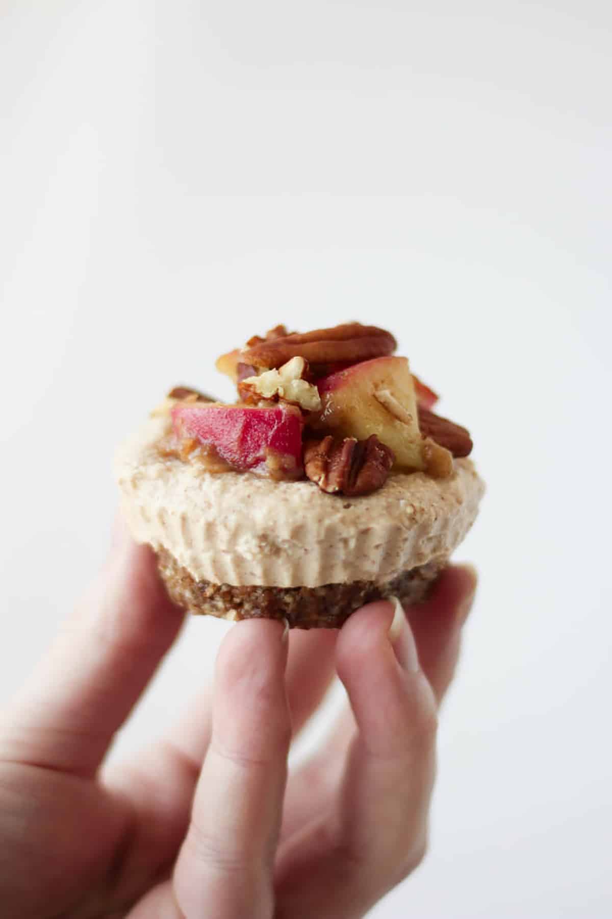 A hand holding up raw vegan cheesecake. 