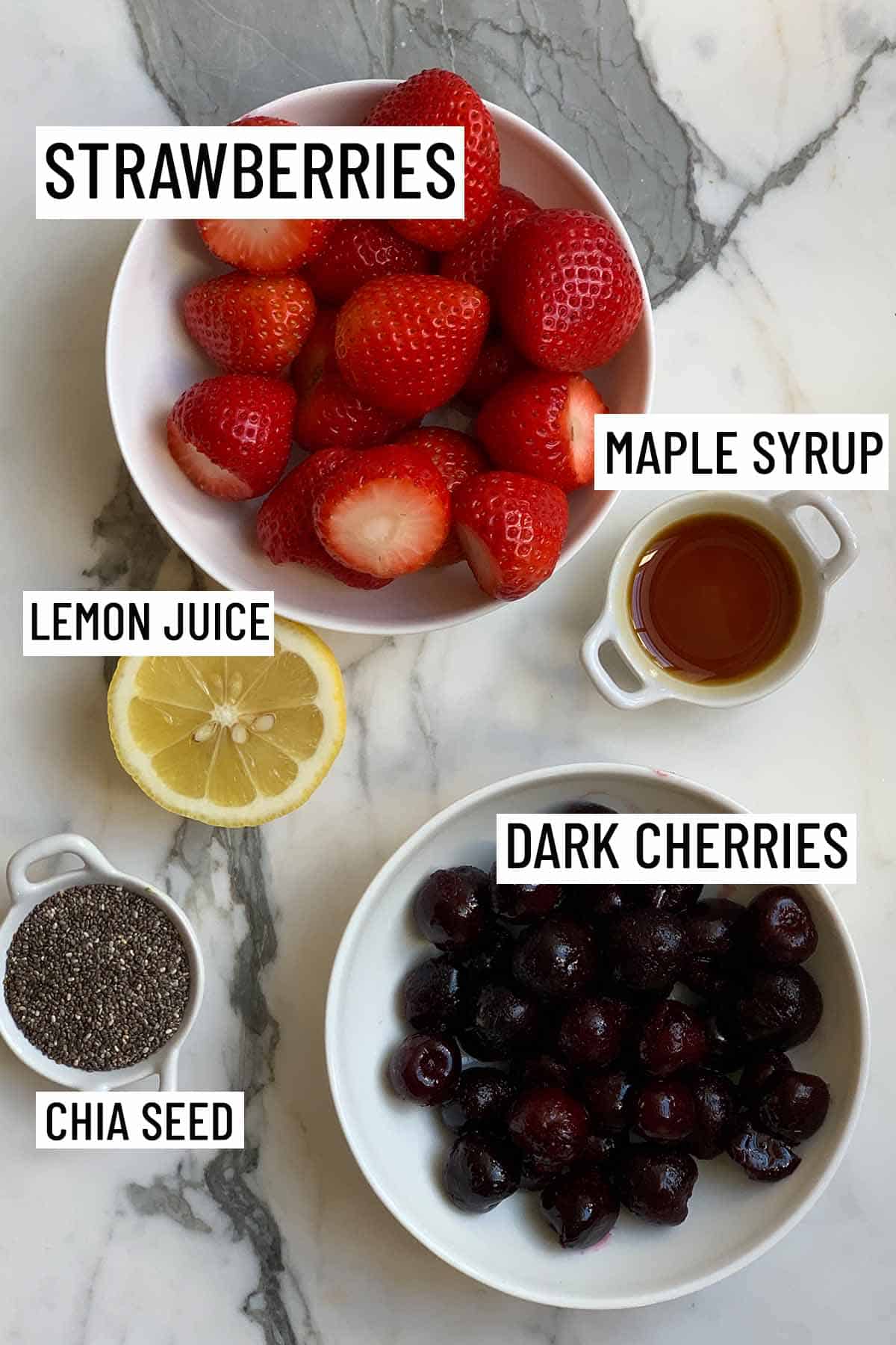 Birds eye view of portioned ingredients needed for recipe including strawberries, cherries, maple syrup, lemon, and chia seed. 